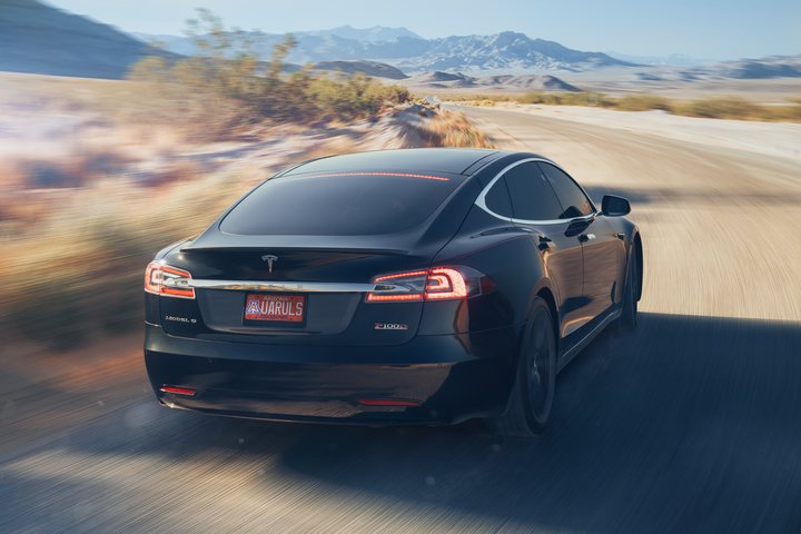 Dark sedan on an open desert road with mountains behind